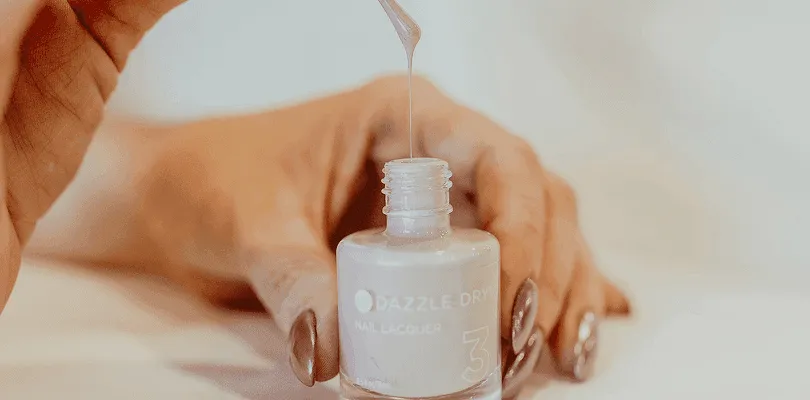 A bottle of Dazzle Dry nail lacquer with polish dripping from the brush above it