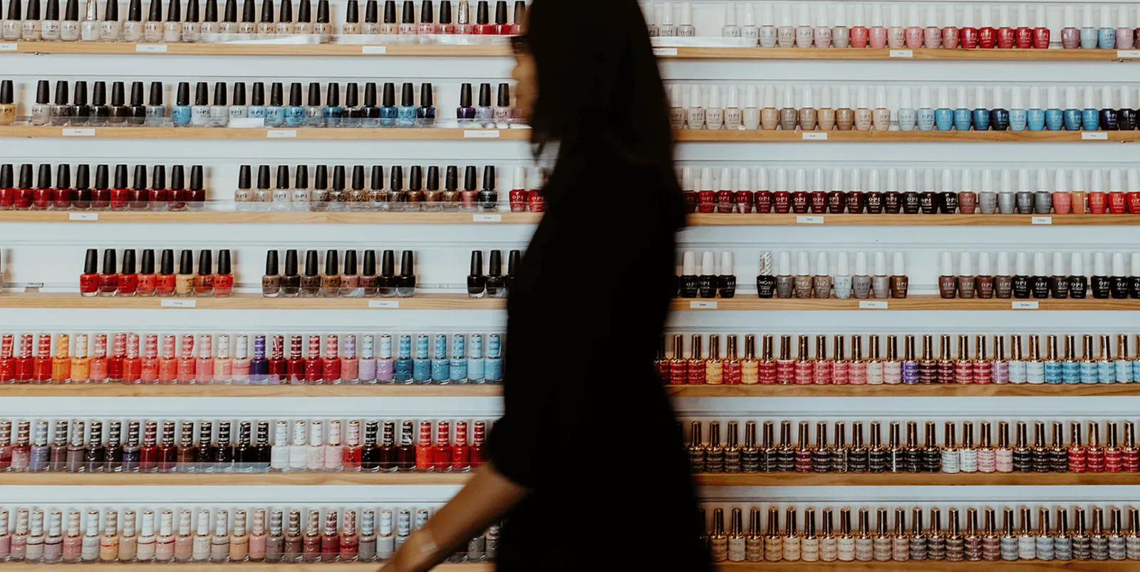 A woman walking past a floor-to-ceiling wall of nail polish colors